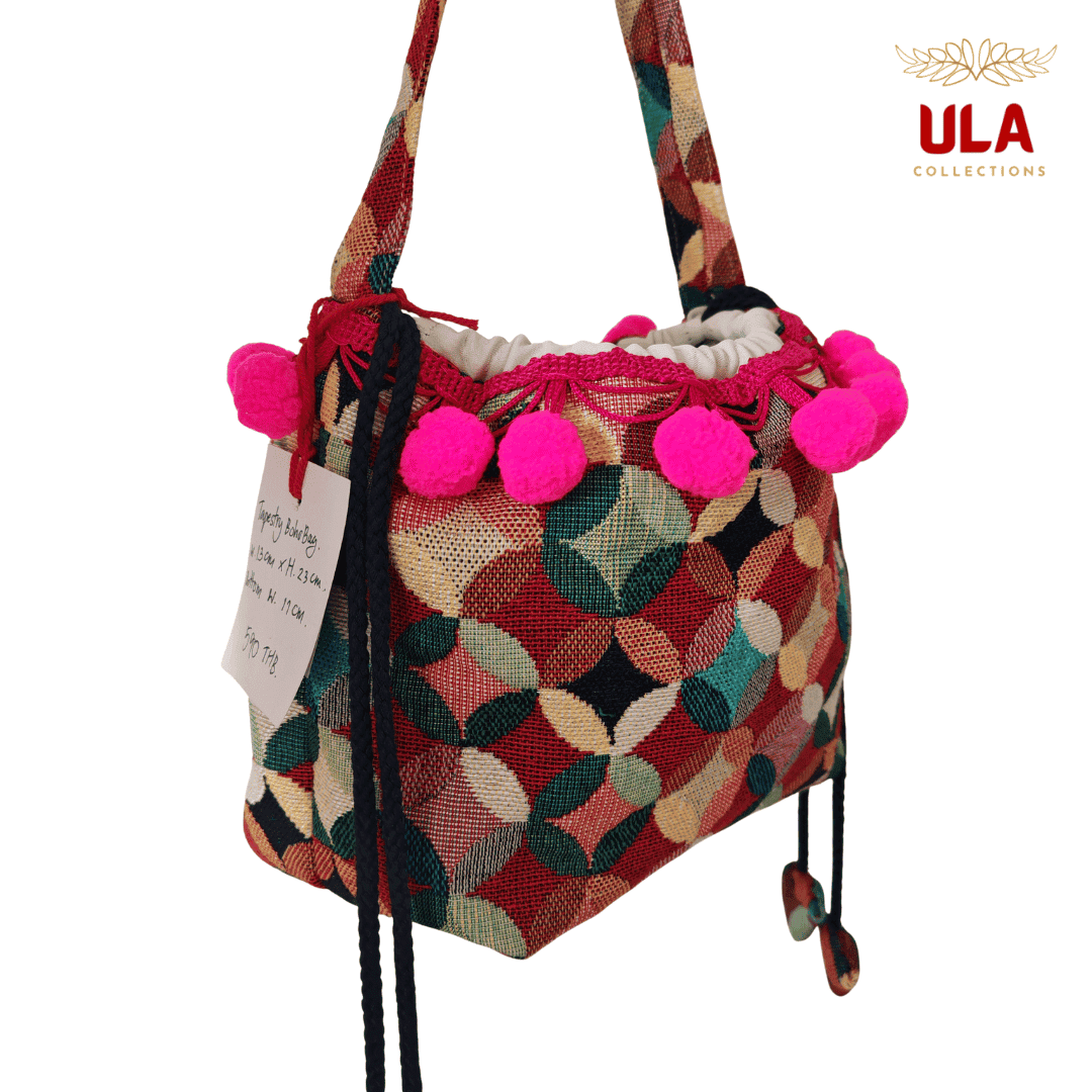 handmade woven drawstring bucket bag with a colorful patchwork/circle pattern in red, green, and cream, featuring hot pink pom-poms.