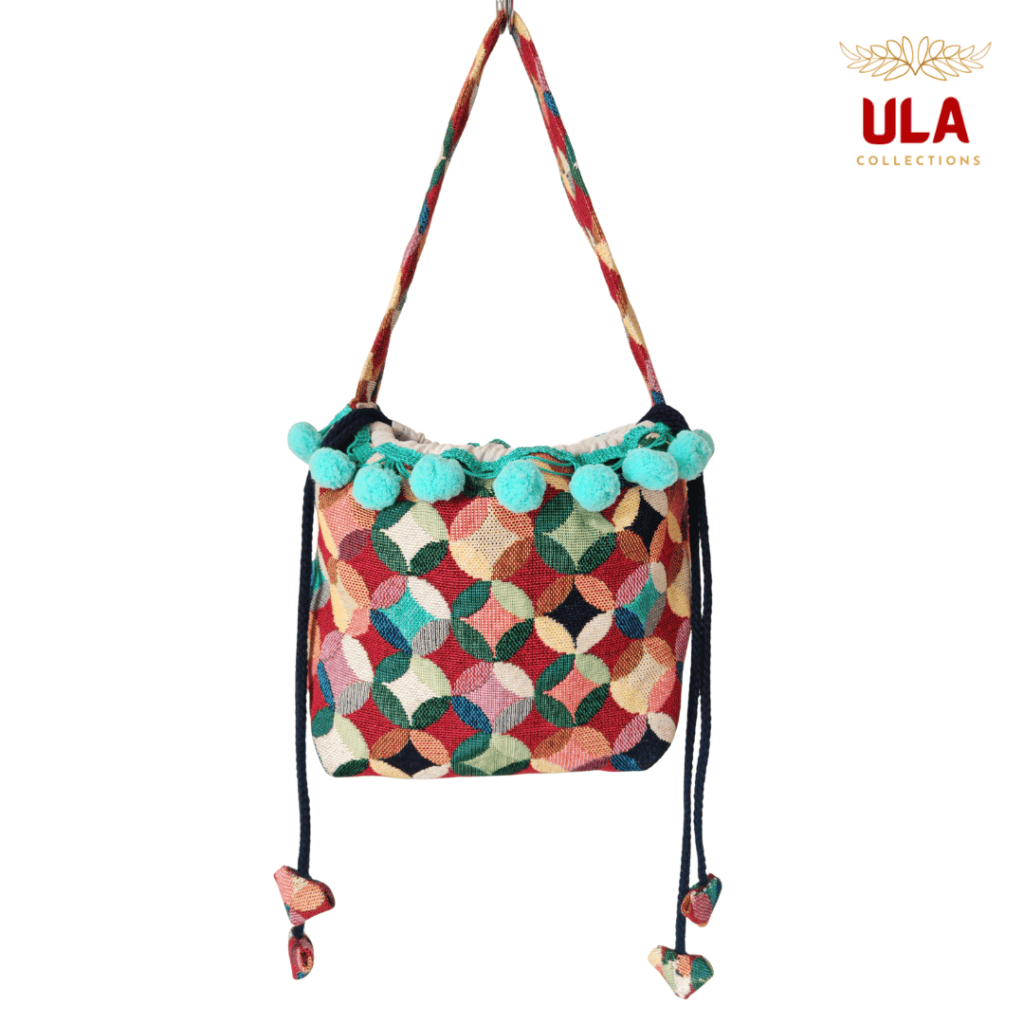 woven colorful patchwork drawstring bag, viewed straight on, featuring teal pom-poms and thick braided drawstrings.