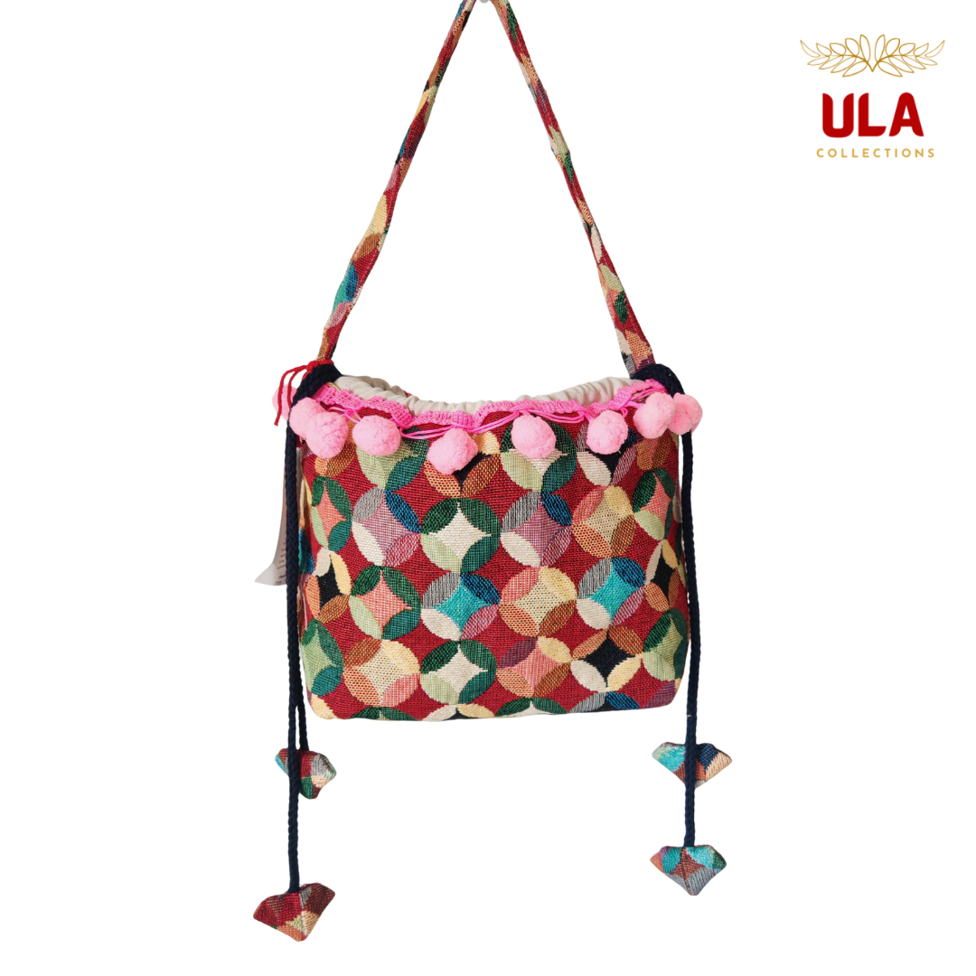 woven colorful patchwork drawstring bag, viewed straight on, featuring soft pink pom-poms and thick braided drawstrings.