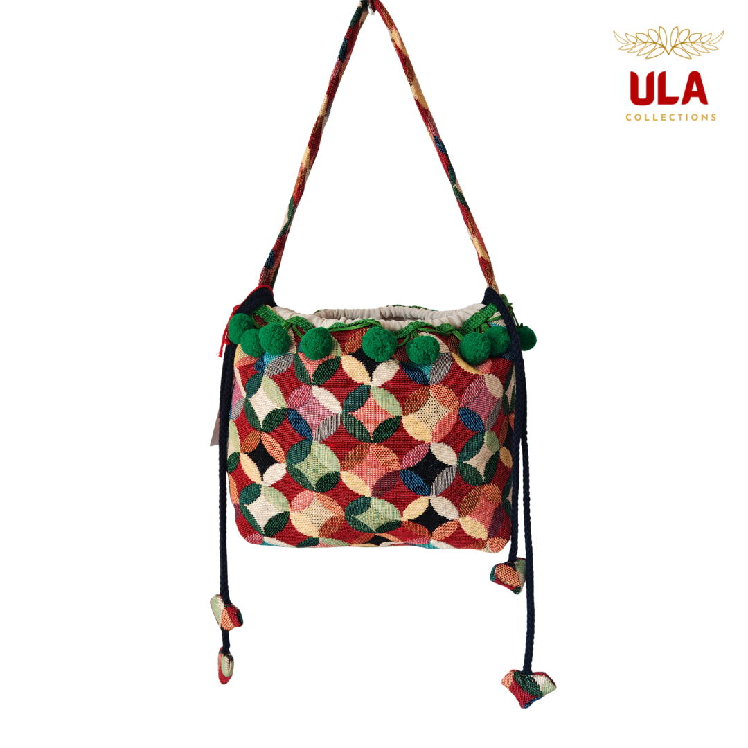 woven colorful patchwork drawstring bag, viewed straight on, featuring dark green pom-poms and thick braided drawstrings.