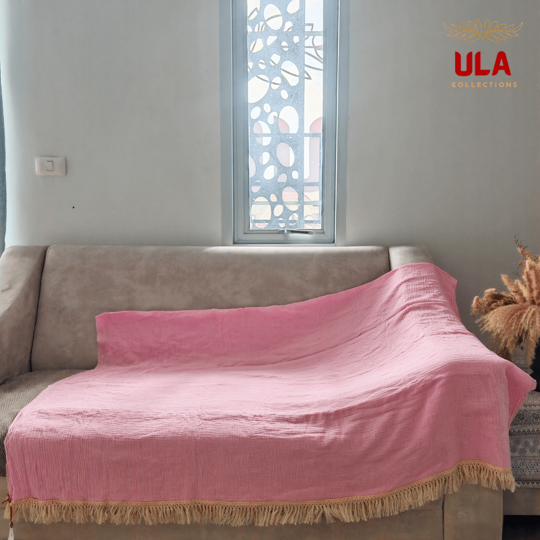 Solid pink (cotton candy) textured throw blanket with thick fringe, draped over a neutral beige sofa with a brown herringbone cushion cover.