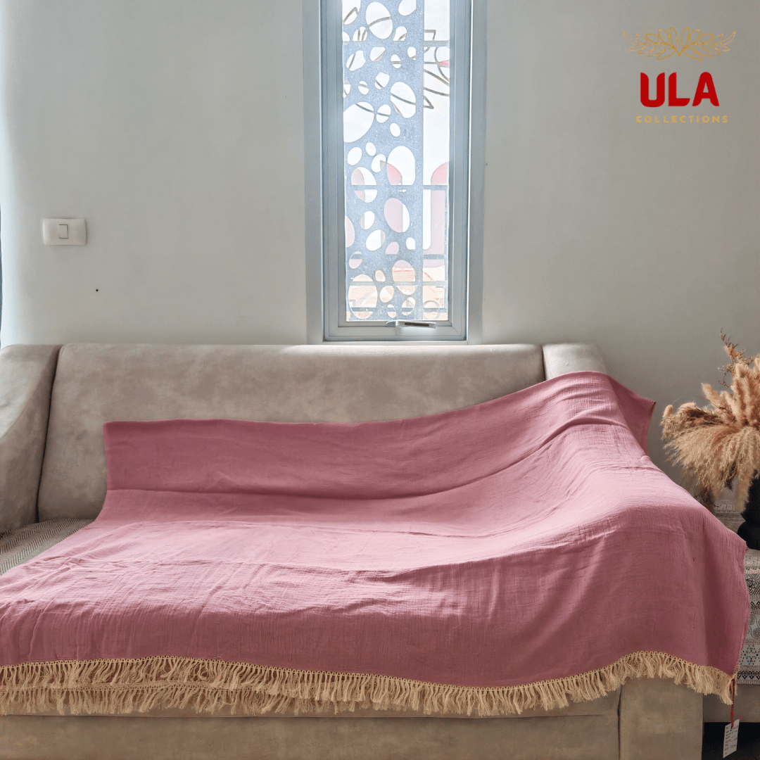Solid rose/dusty blush pink textured throw blanket with thick cream fringe, completely covering a neutral beige sofa.