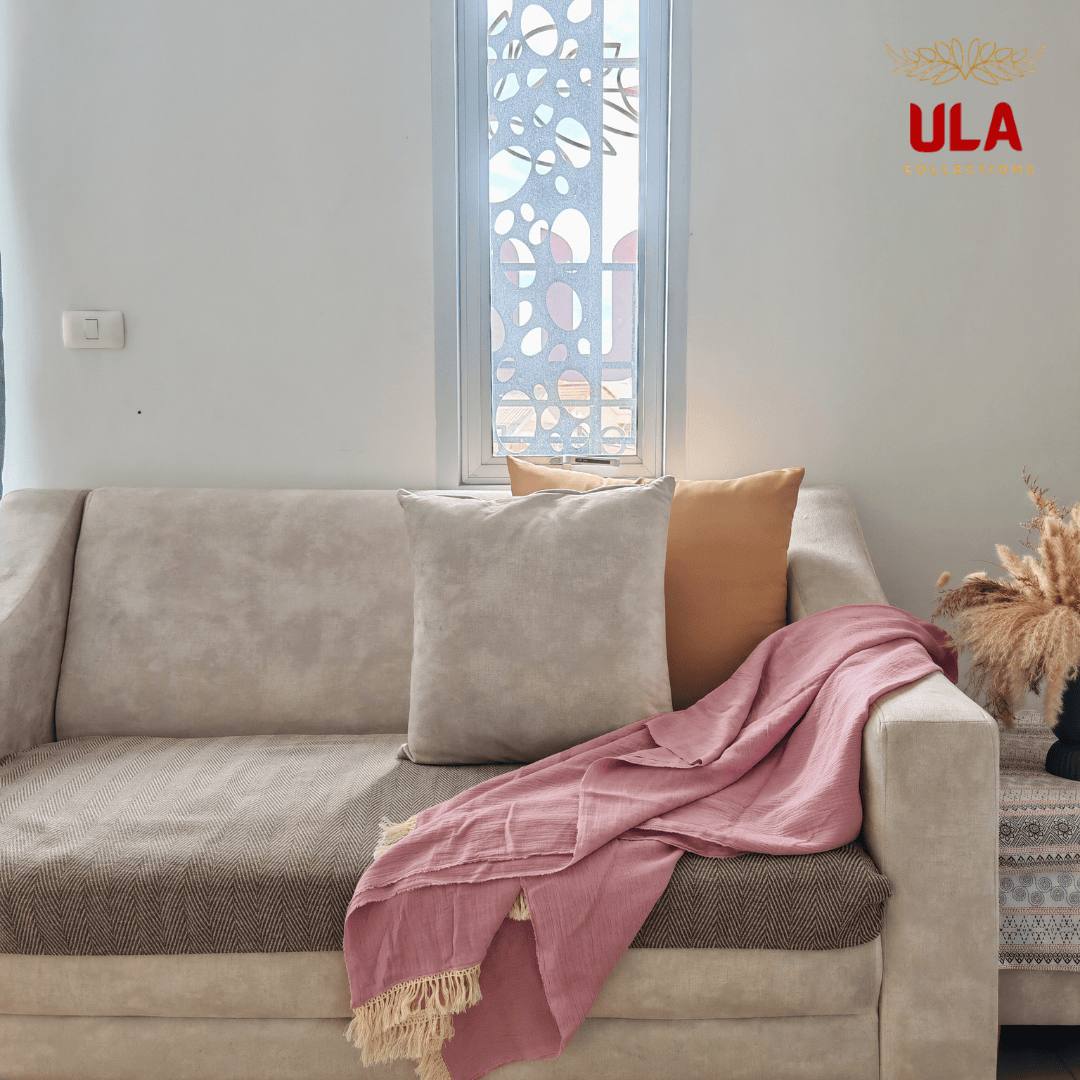 Dusty blush pink crinkle throw blanket with fringe, casually draped over a beige sofa with gray and gold accent pillows.