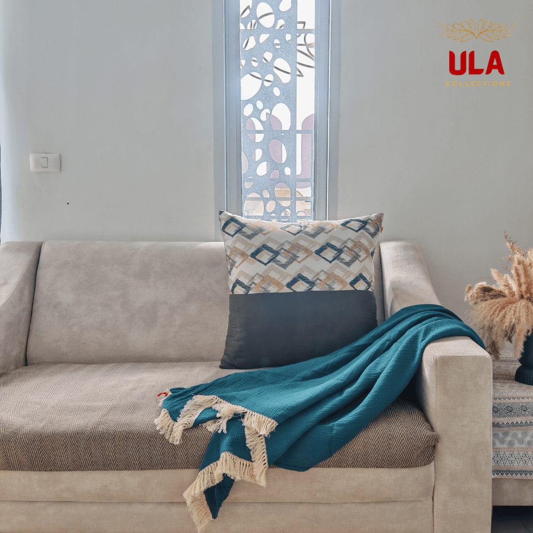 Teal/forest green crinkle throw blanket draped over a beige sofa with a brown herringbone cushion cover and geometric accent pillow.