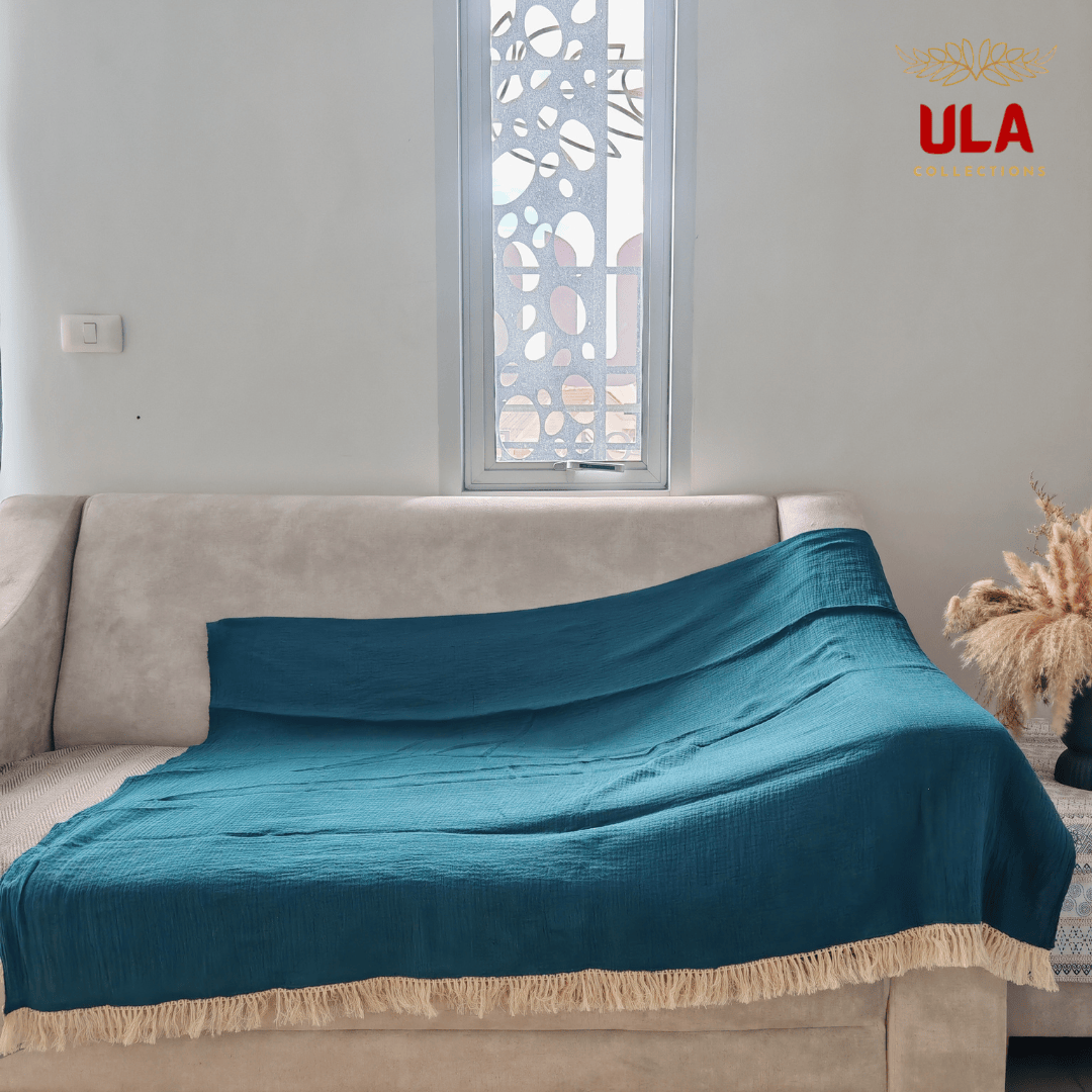 Solid teal/forest green textured throw blanket with thick cream fringe, covering a neutral beige sofa.