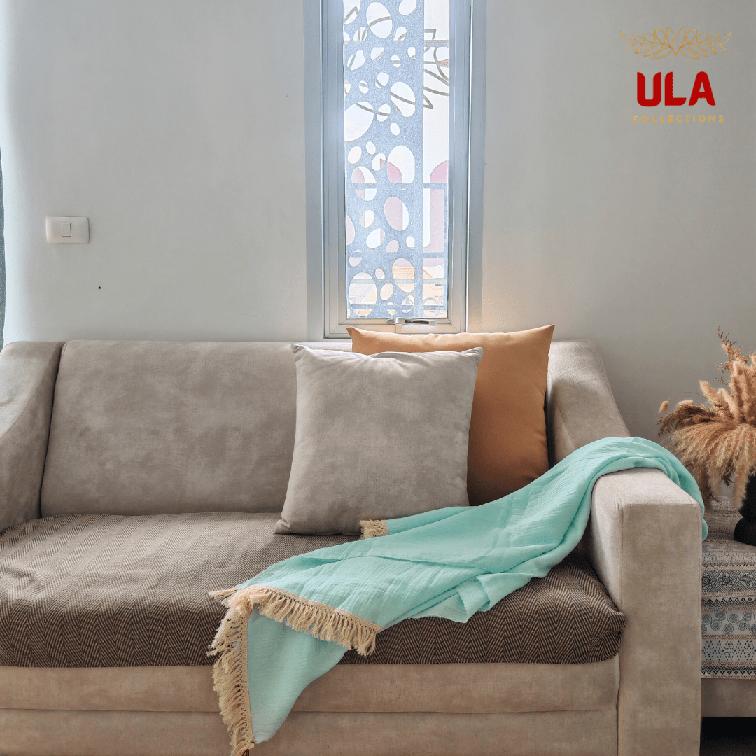 Light blue crinkle throw blanket with fringe, casually draped over a beige sofa with contrasting gray and orange accent pillows.