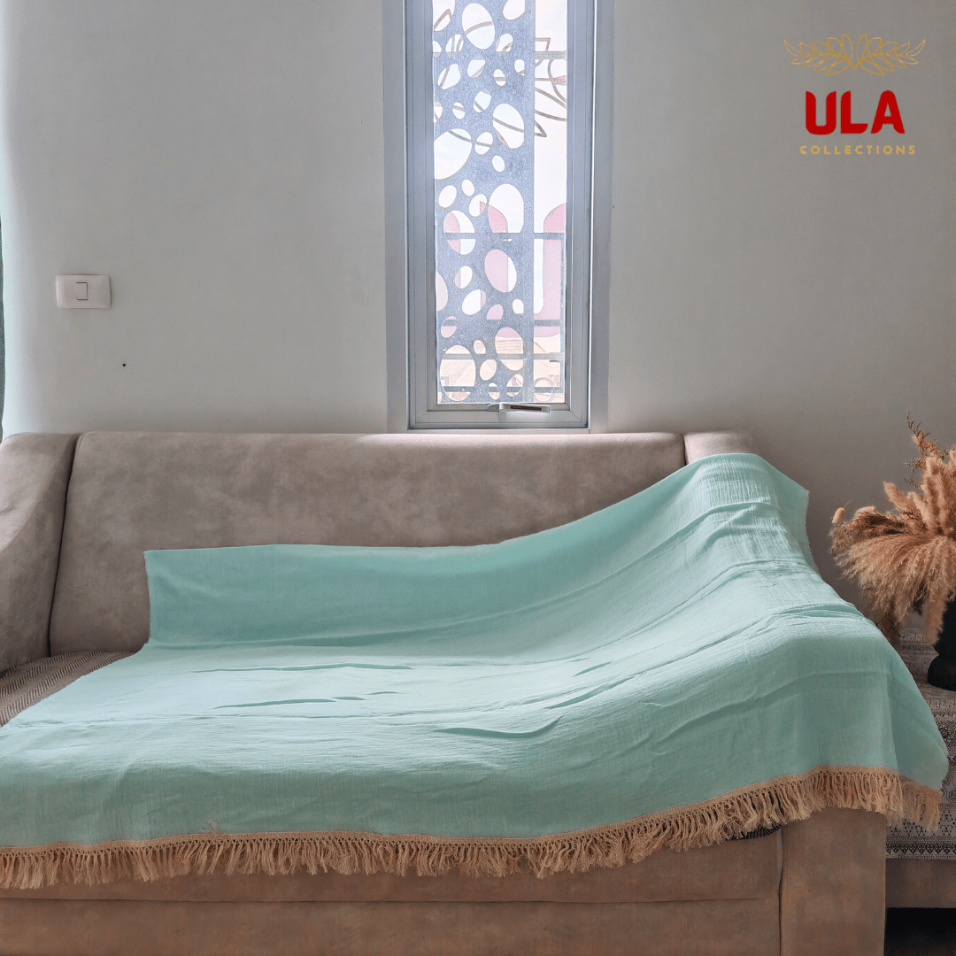 Solid light blue/mint textured throw blanket with thick cream fringe, completely covering a neutral beige sofa.