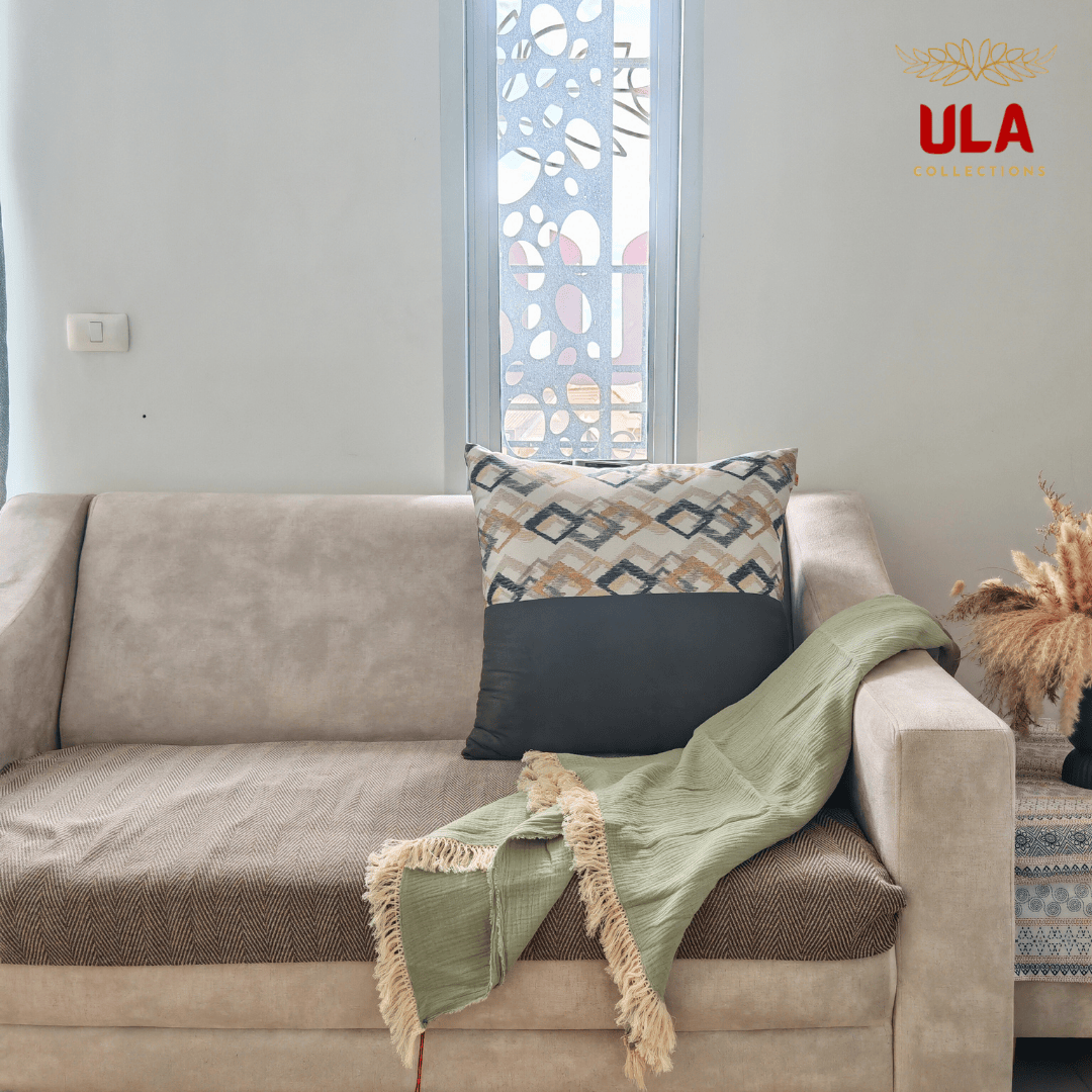 Sage green crinkle throw blanket with fringe, casually draped over a beige sofa with a geometric accent pillow.