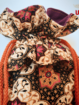 A close-up shot focusing on the upper half of the drawstring bag. The detail highlights the texture of the orange braided cord and the sharp print of the fabric, which includes star-shaped patterns and leaf-like flourishes. The ruffled top shows the transition from the patterned exterior to the solid dark purple fabric lining. The ULA Collections logo is in the top right corner.