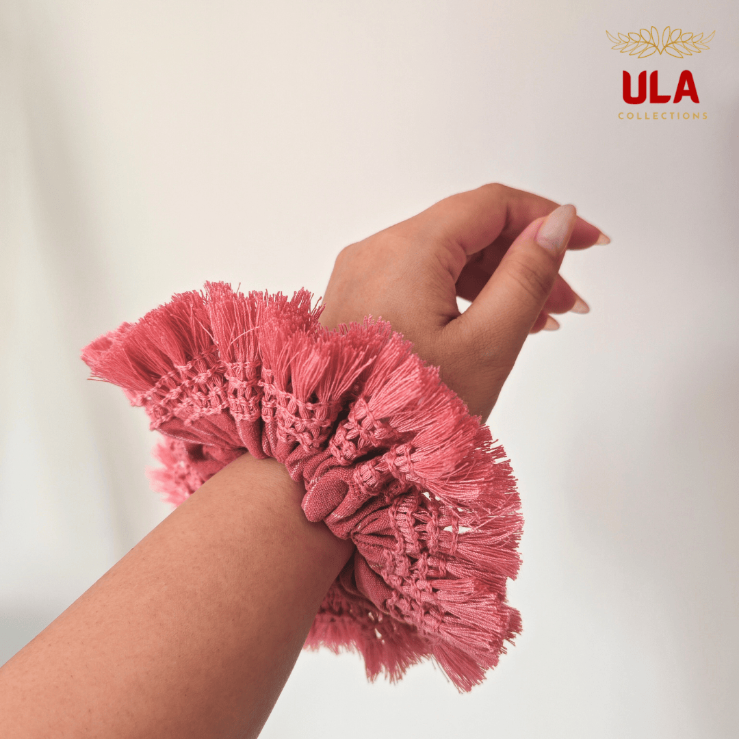 A person's wrist wearing a cotton linen with dusty pink fringe scrunchie