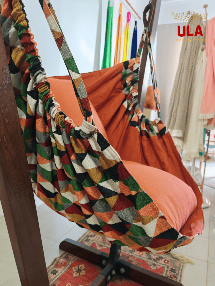 Geometric pattern woven fabric hammock chair with green, orange, and cream triangles and solid orange cushions
