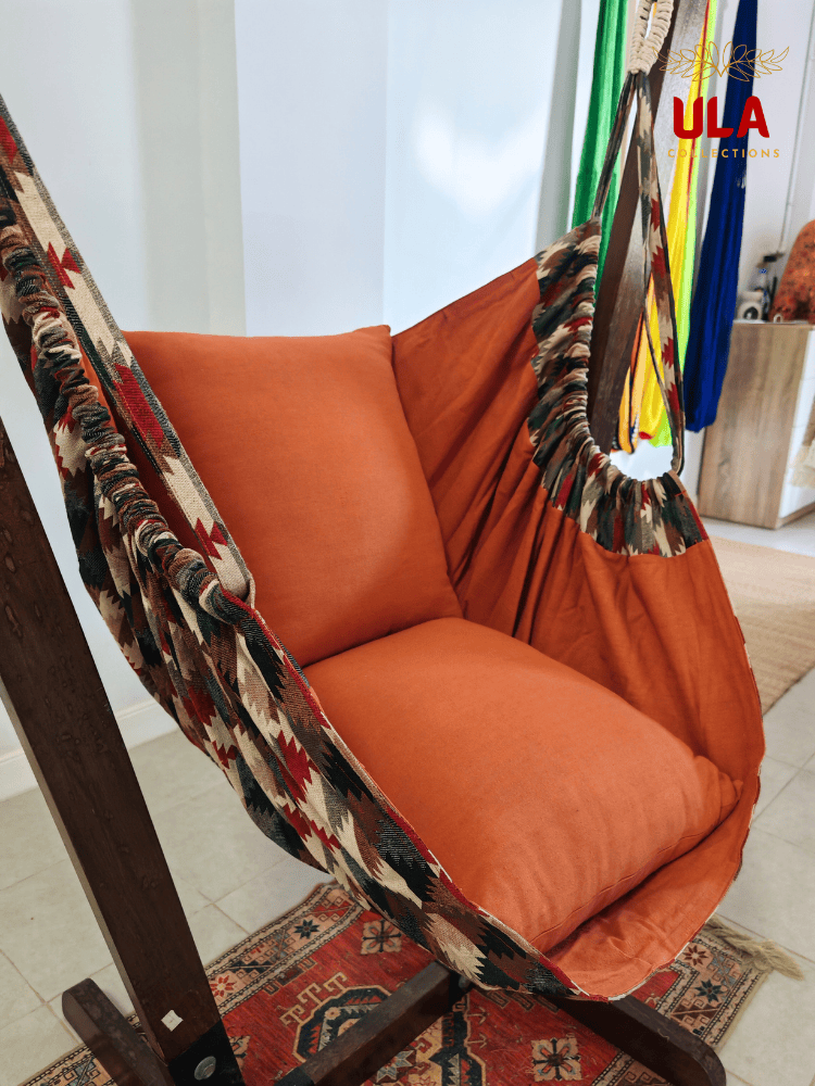 Woven fabric hammock chair with a neutral zigzag pattern in beige, brown, and red, featuring plush orange seat and back cushions.
