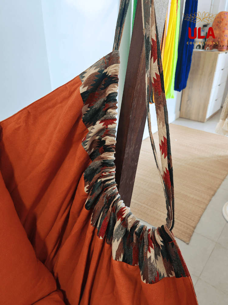 Woven fabric hammock chair with a neutral zigzag pattern in beige, brown, and red, featuring plush orange seat and back cushions.