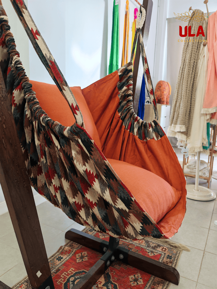 Woven fabric hammock chair with a neutral zigzag pattern in beige, brown, and red, featuring plush orange seat and back cushions.