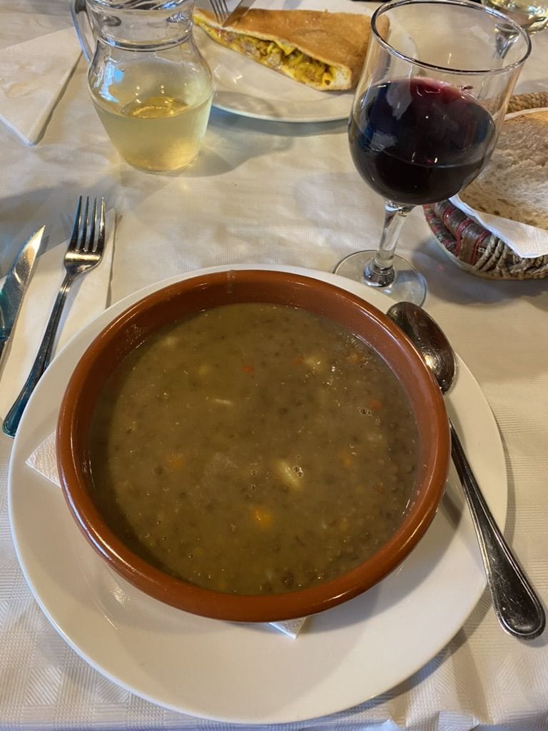 Bowl of lentil stew on a table with a glass of red wine at an albergue in Barbadelo, Spain on the Camino Francés.