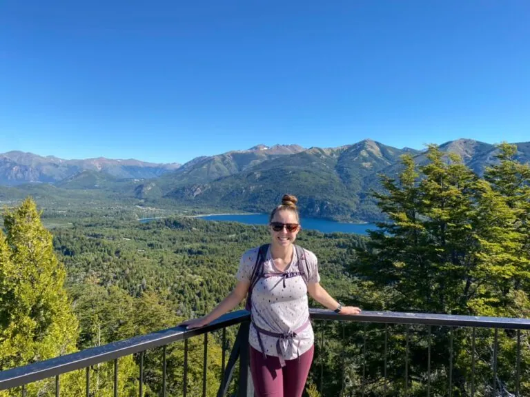 Woman smiling at an overlook of a bright blue lake surrounded by mountains in Bariloche, Argentina