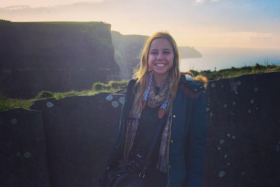 Woman in a coat smiling at the Cliffs of Moher in Ireland