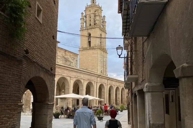 Two people walking down an old city street in front of a cathedral in Los Arcos, Spain
