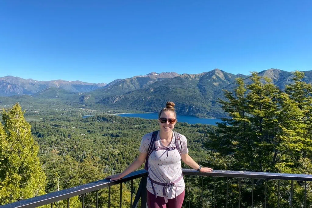 Woman smiling at an overlook of a bright blue lake surrounded by mountains in Bariloche, Argentina