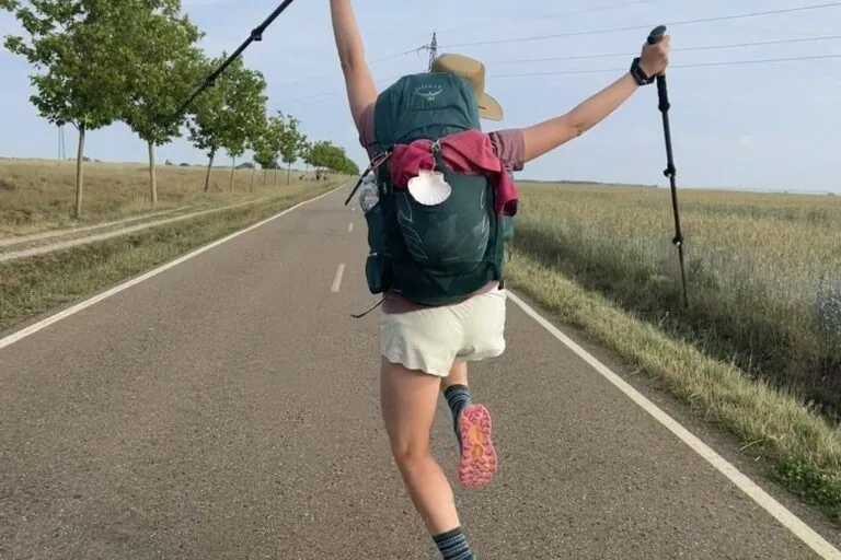 Hiker on an open road jumping up in the air with hiking poles and hands up
