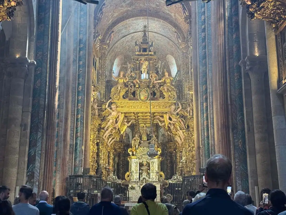 People attending pilgrim's Mass in the cathedral in Santiago de Compostela with an ornate gold altar visible in front of them.