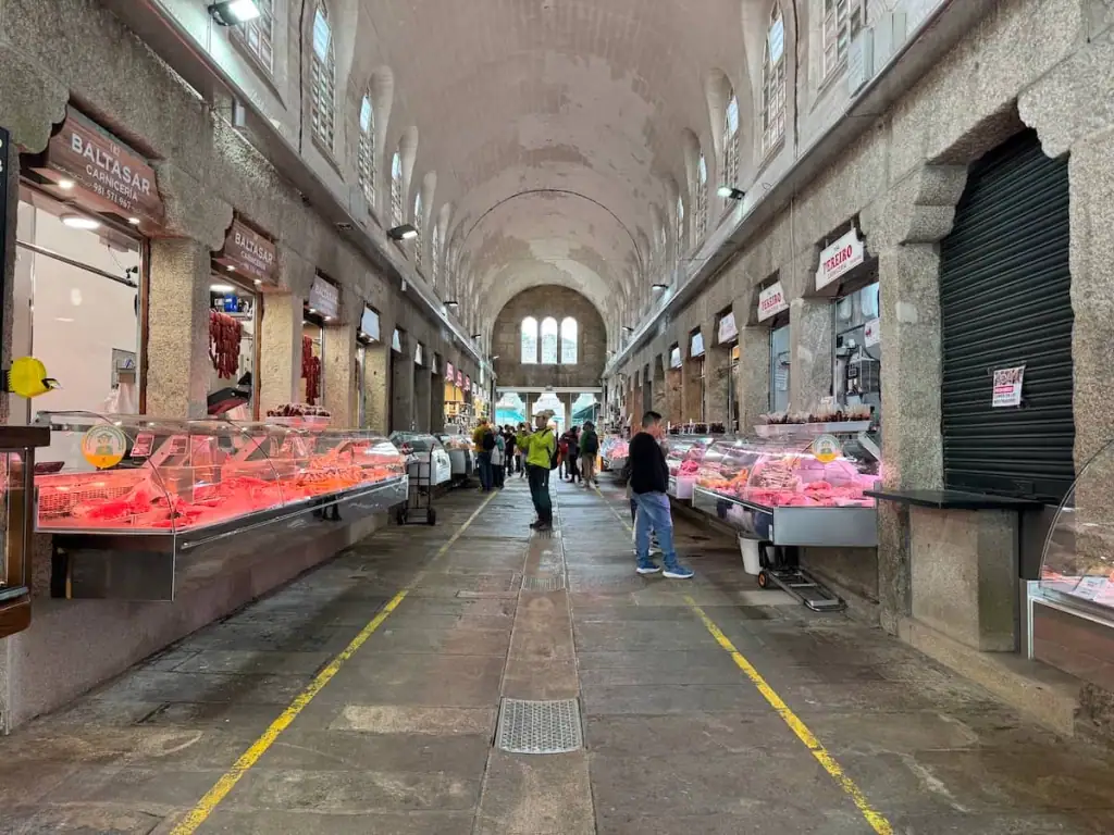 Abastos 2.0 food market in Santiago de Compostela, Spain with stone walls and floors and fresh meat for sale and a few people inside shopping.