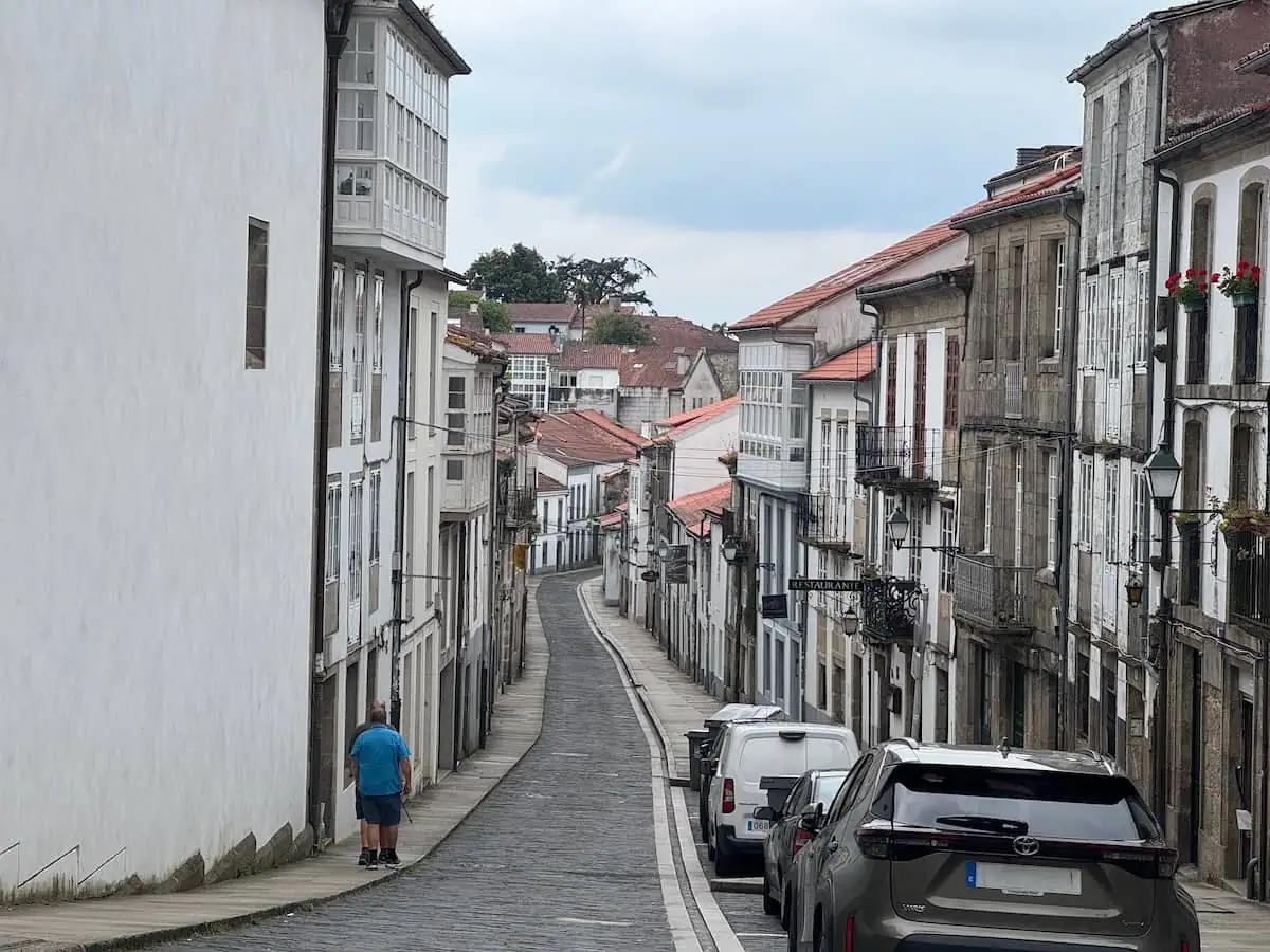 Narrow cobblestone street in Santiago de Compostela, Spain with one man walking on the left.