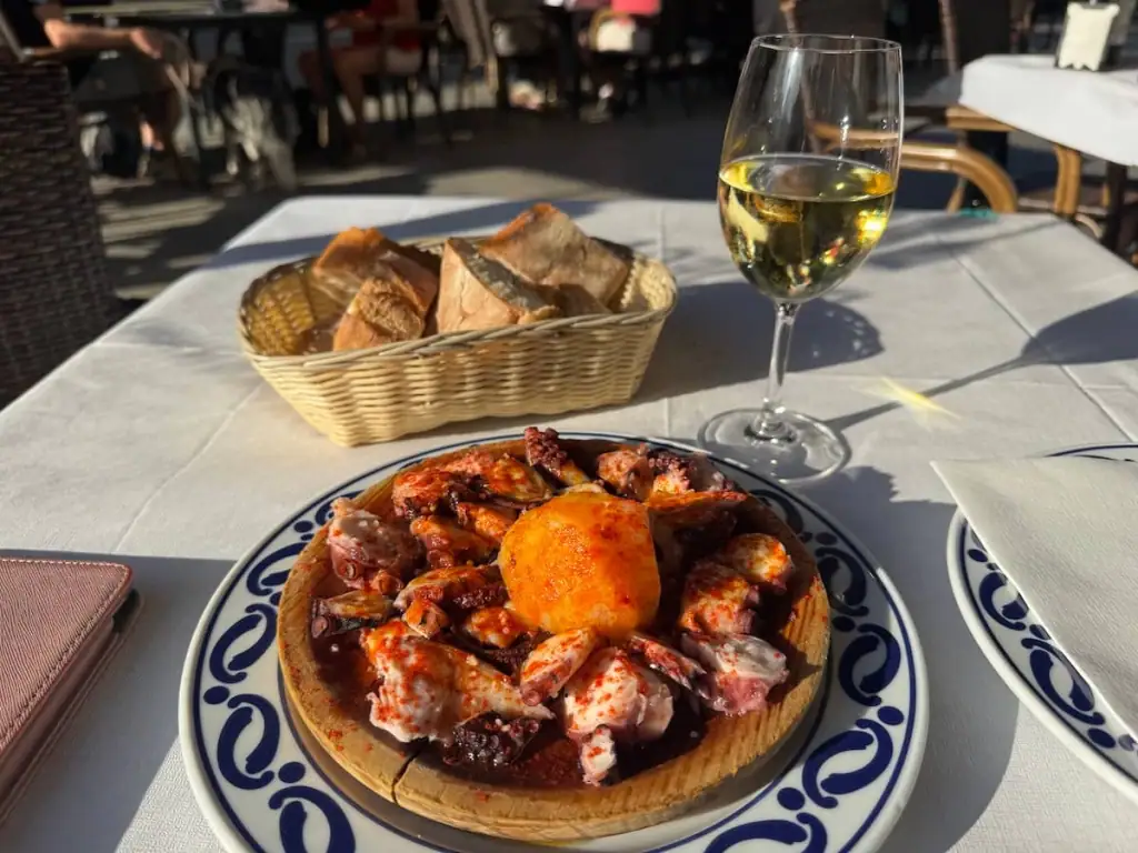 Plate of octopus, basket of bread, and glass of albariño white wine on an outdoor table in Vigo, Spain.