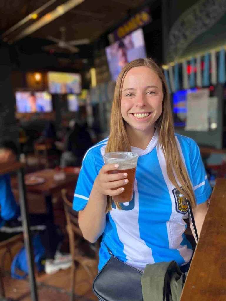 Woman smiling wearing a Messi Argentina jersey and holding a beer