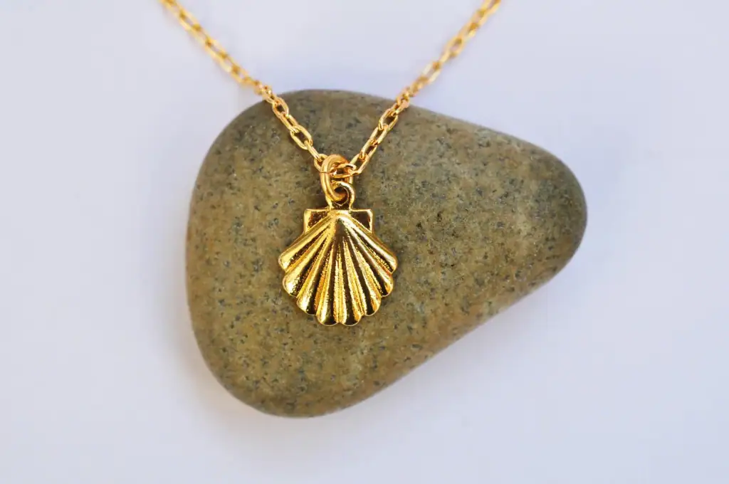 Gold necklace with a Camino scallop shell sitting over a small rock.