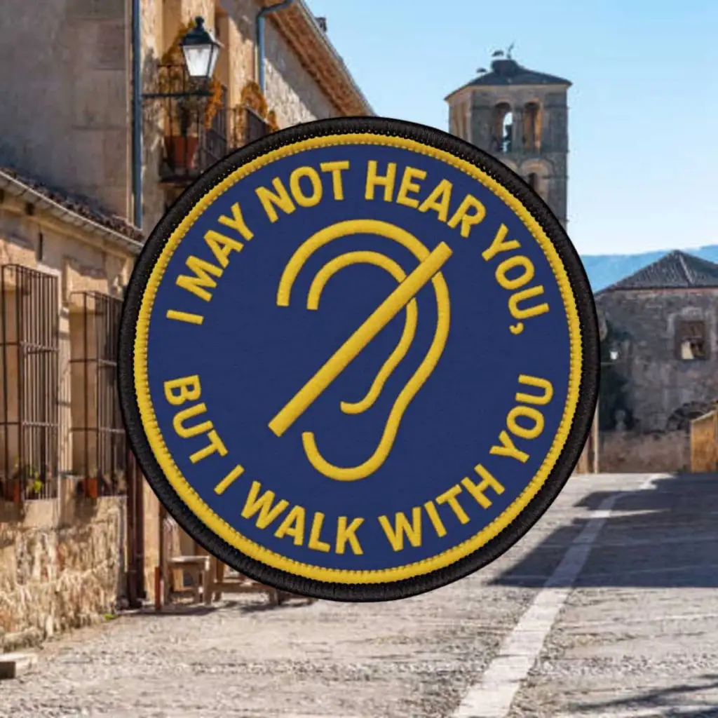 Blue patch showing an ear crossed out that says, "I may not hear you, but I walk with you"