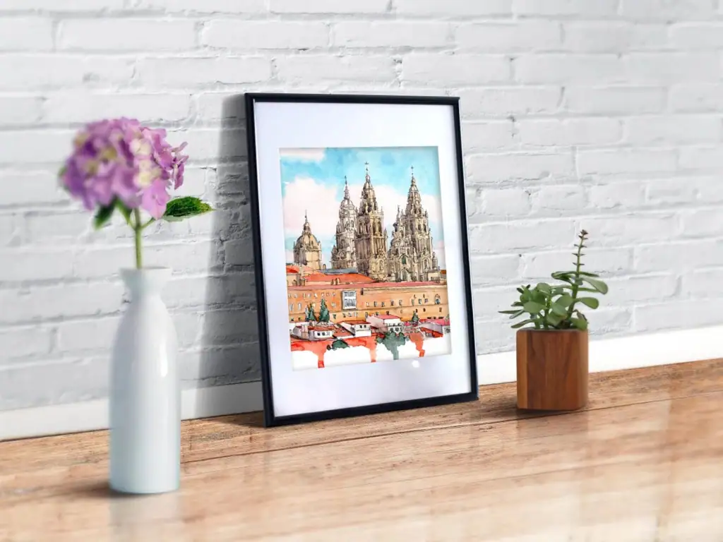 Watercolor painting of the cathedral in Santiago de Compostela shown in a mockup on a desk.