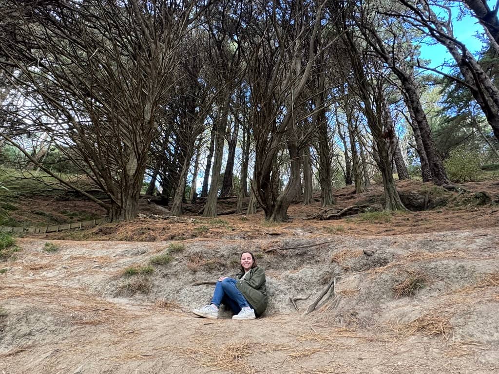 Mikala smiling in a little dug out area under a path in a forest.