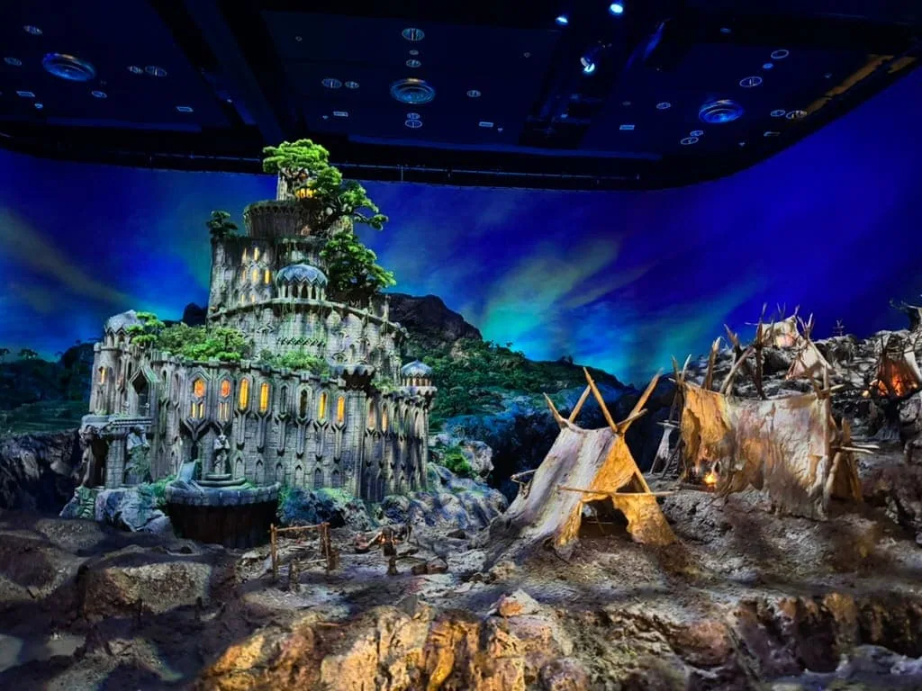 Miniature model of a landscape including a lush green towering castle and tribal huts.