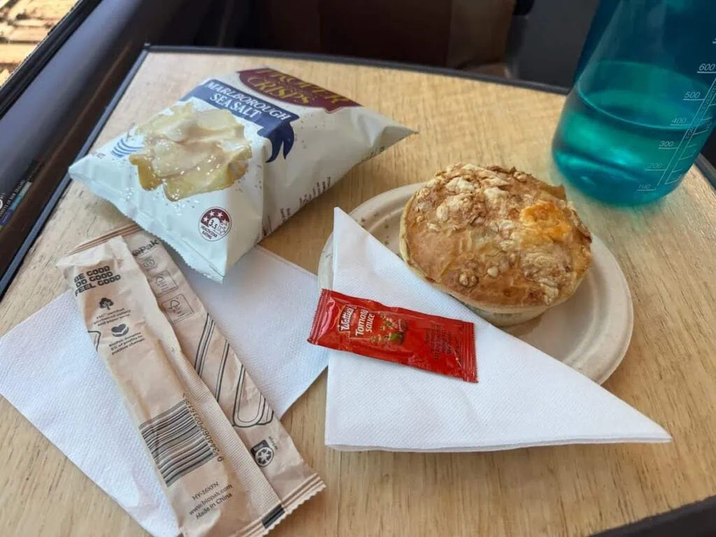 Meat pie on a plate with chips, a water bottle, napkin, and silverware on a train.