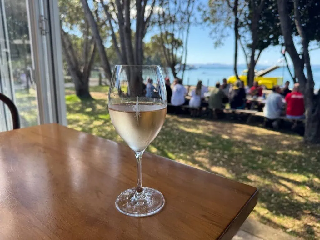 Glass of rose on a table with views of vibrant blue green waters outside at Man O' War Vineyard in Waiheke Island, New Zealand.