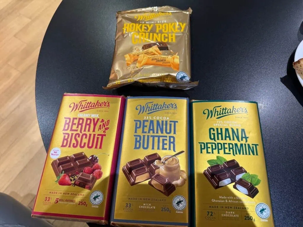 Whittaker's chocolate bars on a table with the following flavors: Berry and a Biscuit, Peanut Butter, Ghana Peppermint, and Hokey Pokey Crunch.
