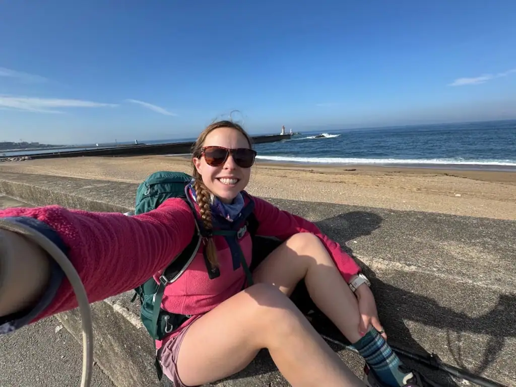 Mikala smiling in a selfie sitting along a bench next to the ocean where the river out of Porto meets the ocean.