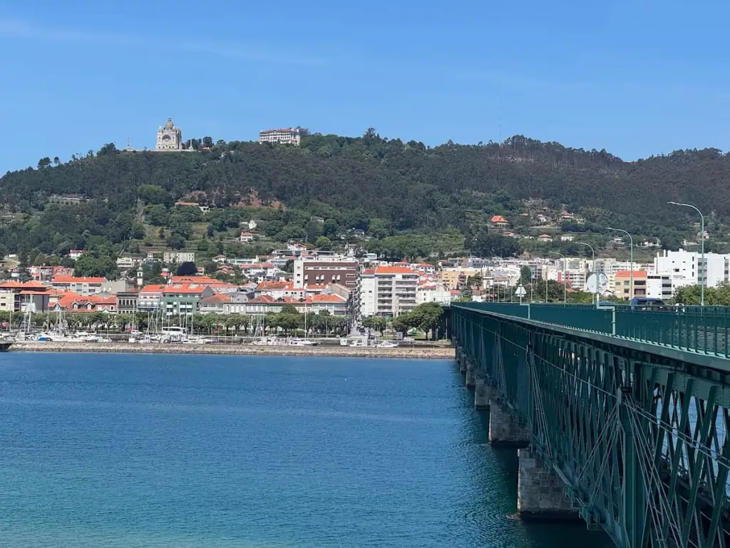 Ponte Eiffel bridge on the right leading into Viana do Castelo over bright blue green water and with the city in the distance built up on a big hill.