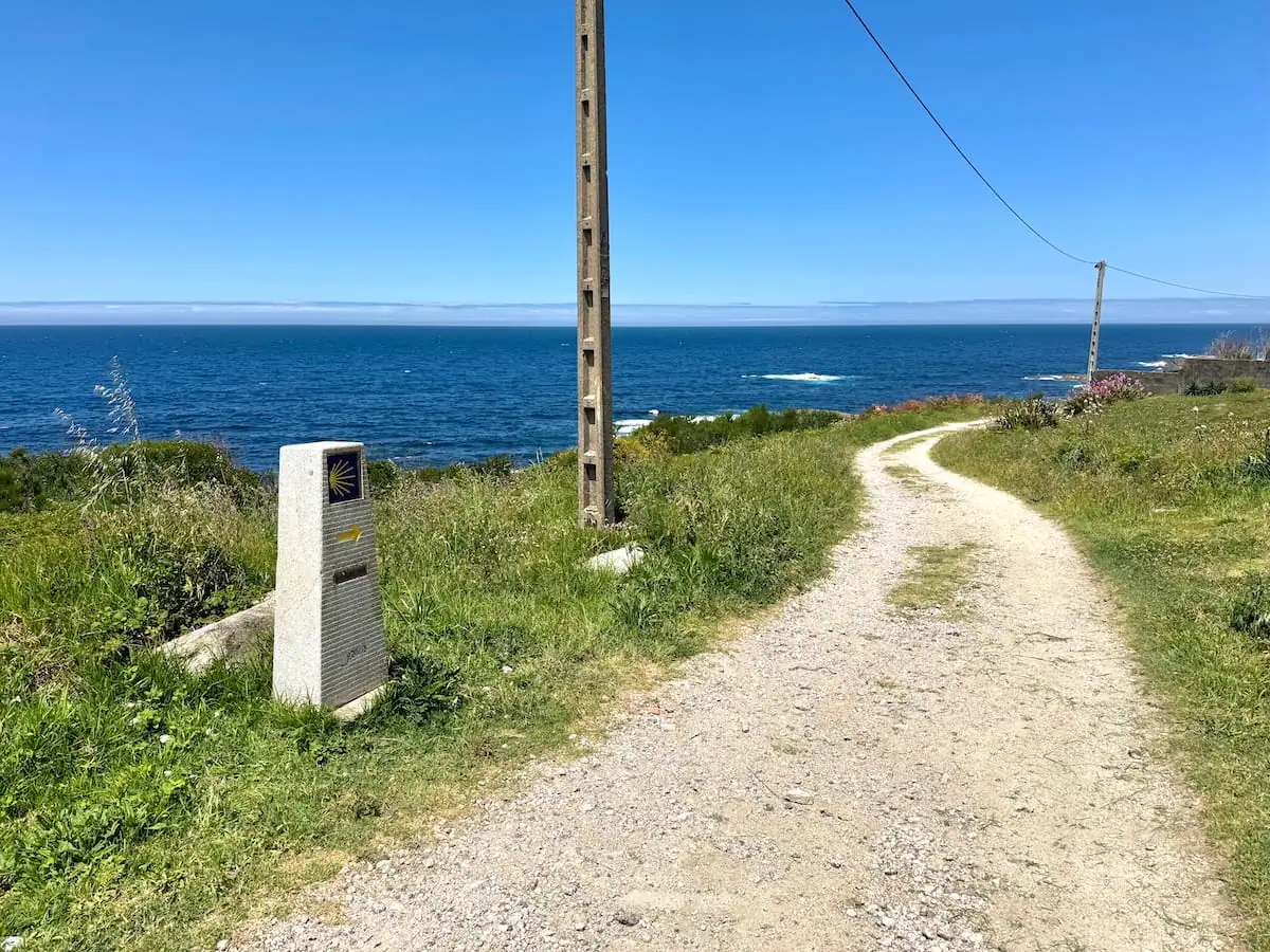 Camino Portugués Coastal path stretching ahead through some grass with views of the ocean below and a trail marker next to the path.