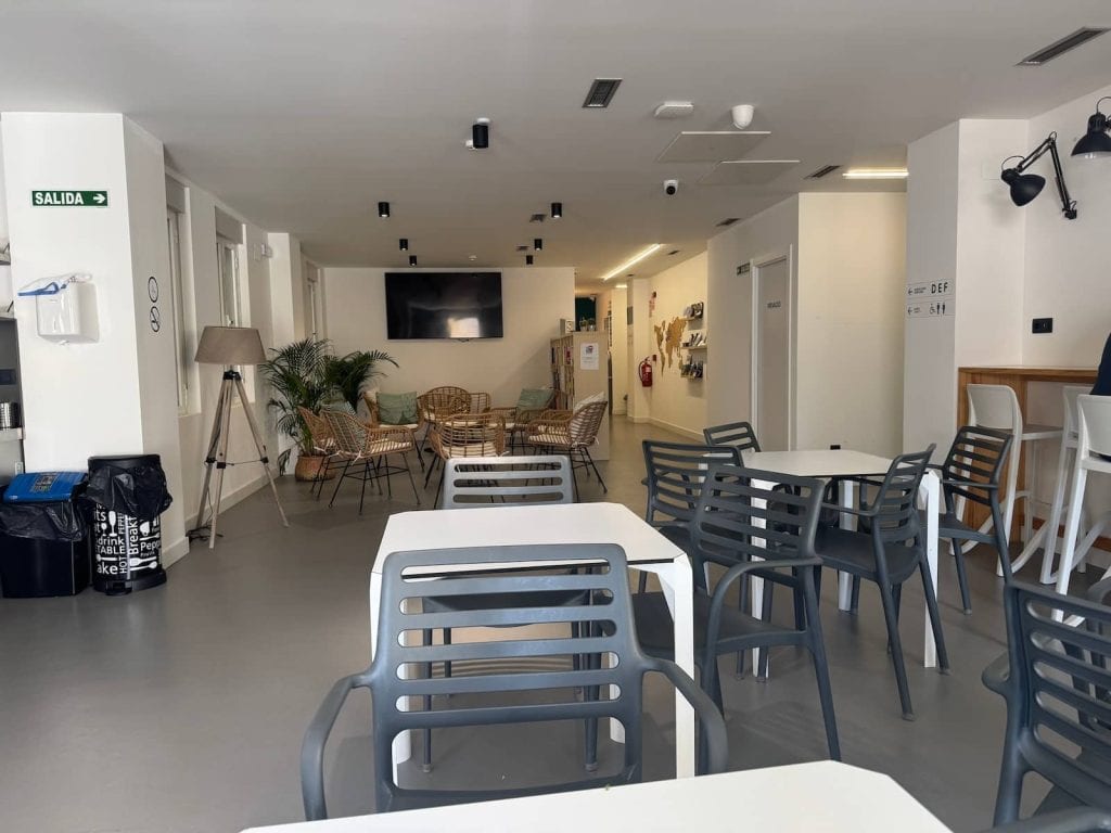 Tables and chairs in a kitchen area and then couches and a TV farther back at Bulezen Urban Hostel in Pontevedra along the Camino Portugués.