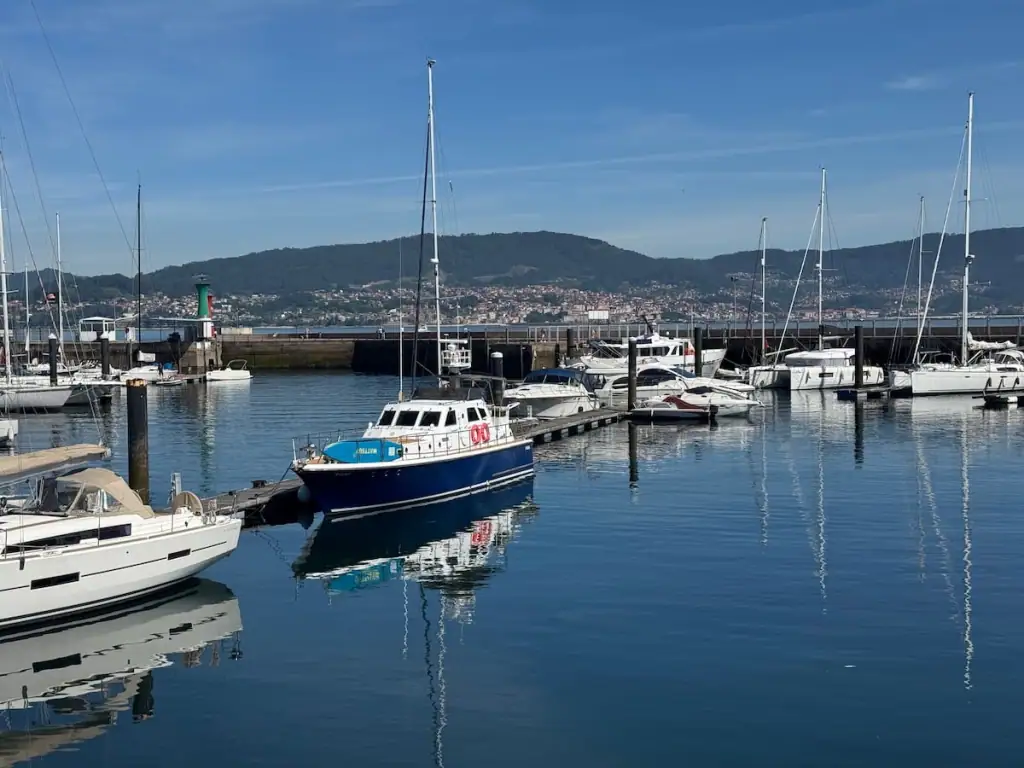 Boats on the water in Vigo with other towns built up on hills visible in the distance.