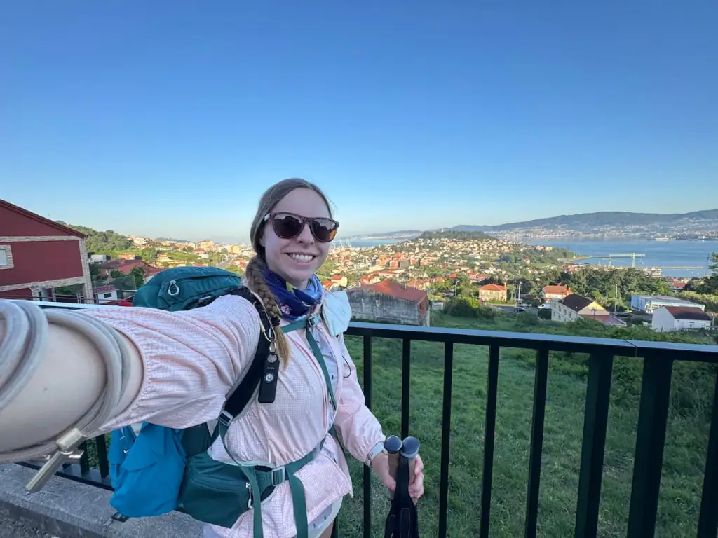 Mikala smiling in a selfie with a viewpoint of the area surrounding Vigo below with lots of buildings, water, and small mountains.