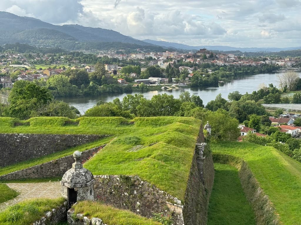 Fortress in Valença covered in lush green grass with a view of Tui and mountains over the river in the distance.