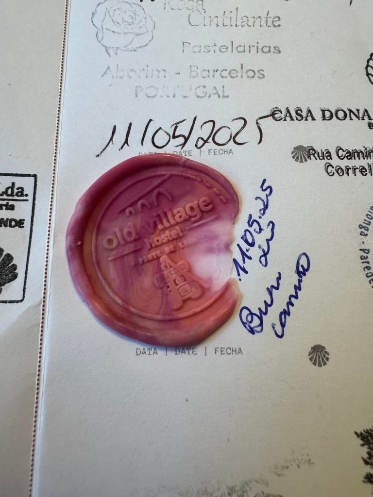 Multicolor pink wax stamp in a Camino pilgrim passport that says "Old Village hostel" and shows a pilgrim backpack.