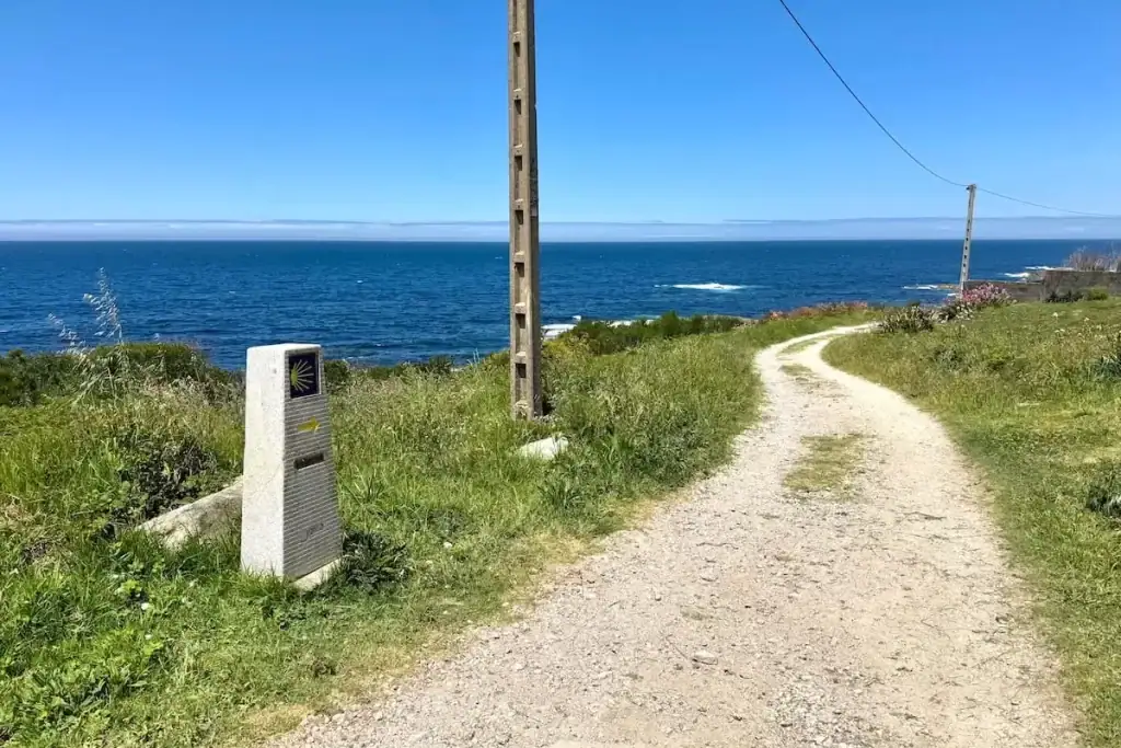 Camino Portugués Coastal path stretching ahead through some grass with views of the ocean below and a trail marker next to the path.