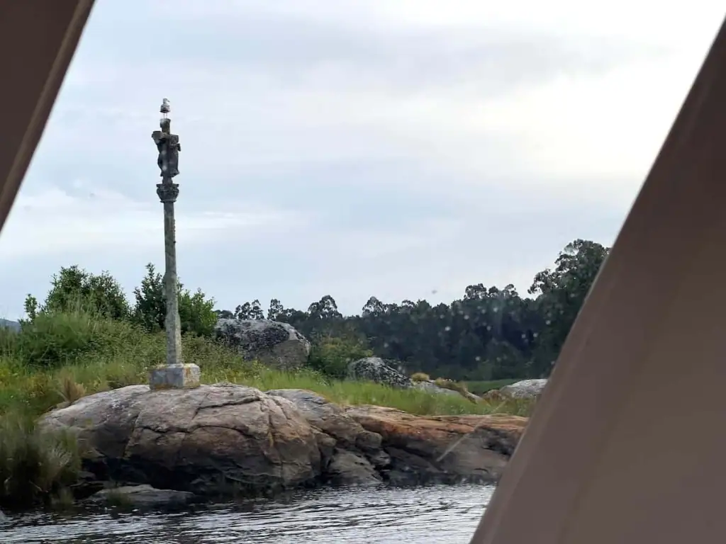 Cross on top of a rock alongside water with a seagull perched on top. During the boat ride on the Camino Spiritual Variant, you pass by 12 crosses.