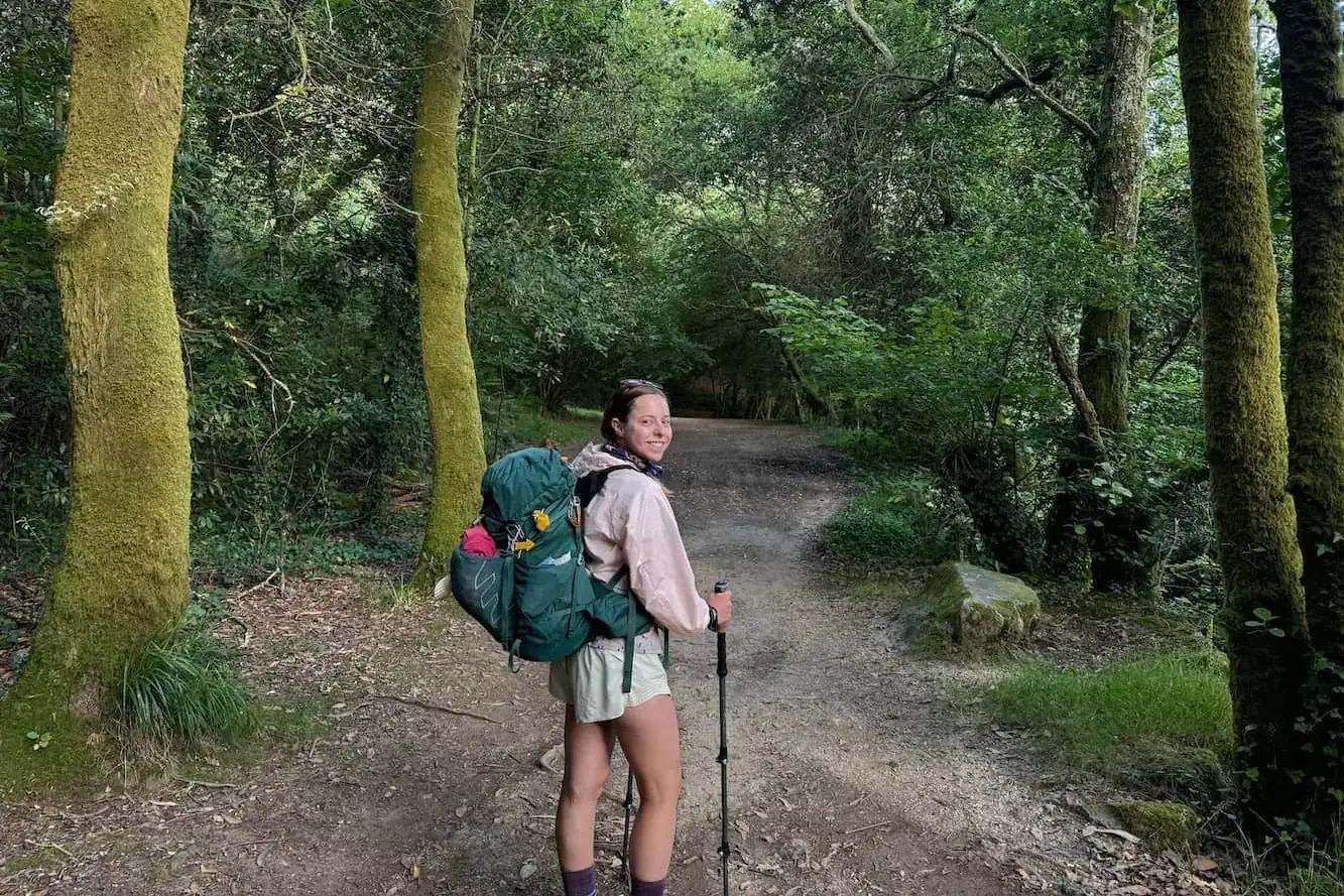 Mikala walking in a lush green forest along the Spiritual Variant on the Camino Portugués and turning back to smile at the camera.