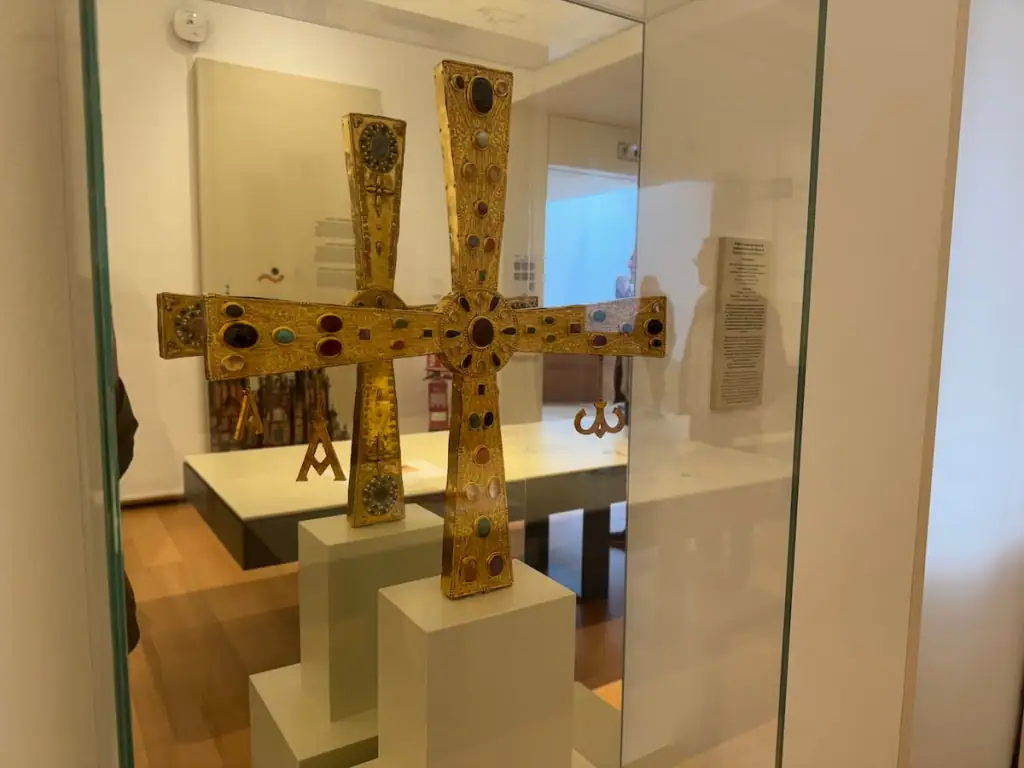 Replica of a gold cross with an even height and width and jewels embedded in it.