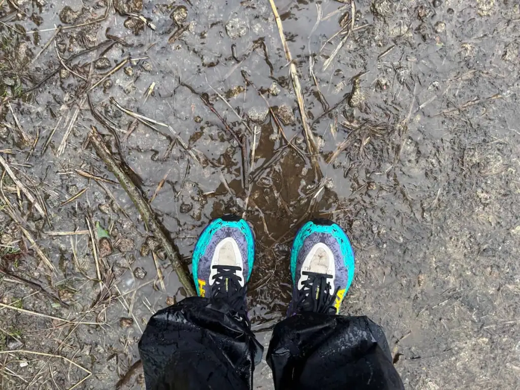 Two feet wearing Hoka Speedgoats and standing on a very wet path on the Camino on a rainy day.